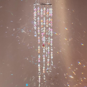 May include: A hanging mobile featuring a circular silver metal frame with multiple cascading strands of translucent beads in shades of pink, yellow, and clear. Each strand terminates in a faceted teardrop-shaped crystal pendant.