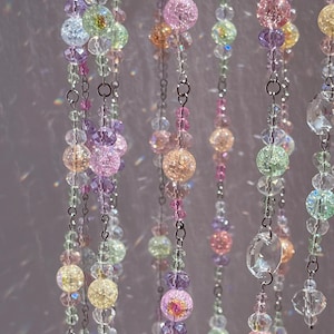 May include: Multiple vertical strands of decorative beads suspended on thin silver-toned metal chains. The beads feature a mix of translucent, faceted clear crystals and round crackled glass spheres in pastel shades of pink, yellow, green, and purple.