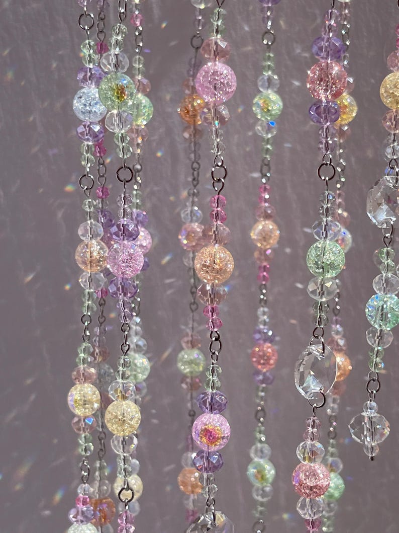 May include: Multiple vertical strands of decorative beads suspended on thin silver-toned metal chains. The beads feature a mix of translucent, faceted clear crystals and round crackled glass spheres in pastel shades of pink, yellow, green, and purple.