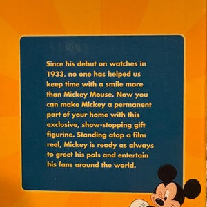 May include: A box with a blue panel featuring text about Mickey Mouse and a cartoon image of Mickey. The box is orange and has the Lorus logo at the bottom. The text mentions Mickey's debut on watches in 1933.