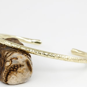 May include: A gold hammered bangle bracelet. The bracelet is made of thick, textured metal and has a simple, elegant design.