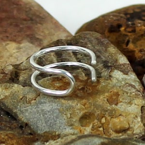 May include: A silver nose ring with a simple, twisted design. The ring is made of a single piece of wire that is twisted into a loop.