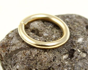 May include: A gold-colored seamless ring, also known as a captive bead ring, is shown on a rough, gray rock surface.