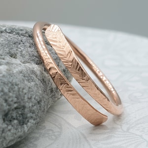 Op de afbeelding: Een roségouden ring met een gehammerde textuur. De ring is gemaakt van twee banden die in elkaar gedraaid zijn.