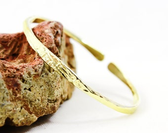 May include: A gold hammered bangle bracelet with a textured surface.
