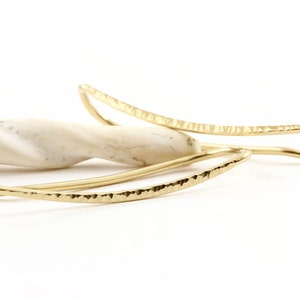 Puede incluir: Un par de pendientes de metal martillado de color dorado con forma curva.
