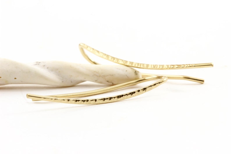 Puede incluir: Un par de pendientes de metal martillado de color dorado con forma curva.