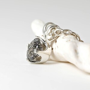 May include: A silver pendant with a clear quartz stone with black inclusions. The pendant is on a silver chain.