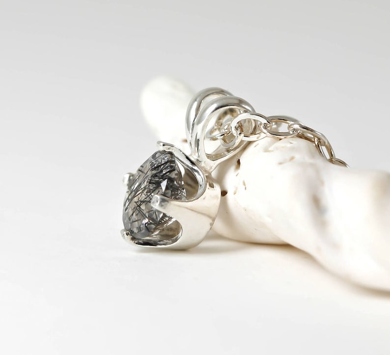 May include: A silver pendant with a clear quartz stone with black inclusions. The pendant is on a silver chain.