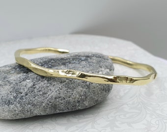 May include: A gold hammered bangle bracelet with a textured finish.