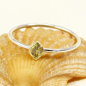May include: A delicate silver ring featuring a gold leaf design. The ring is simple and elegant, ideal for everyday wear.