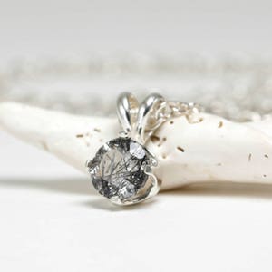 May include: A silver pendant necklace with a round, clear quartz stone with black inclusions. The stone is set in a silver bezel setting.