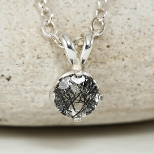 May include: A silver necklace with a round pendant featuring a clear quartz stone with black inclusions. The pendant is set in a silver bezel.