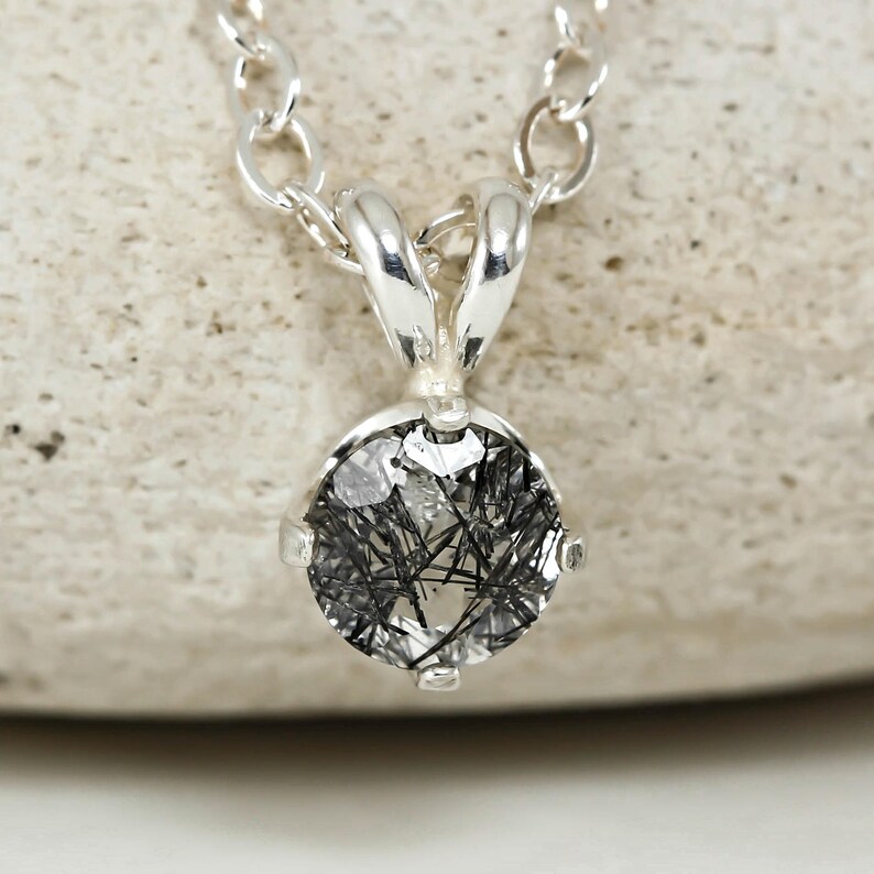 May include: A silver necklace with a round pendant featuring a clear quartz stone with black inclusions. The pendant is set in a silver bezel.