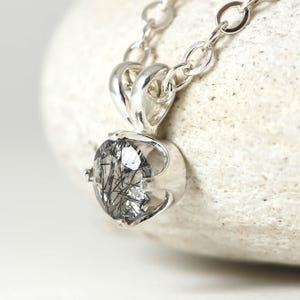 May include: A silver necklace with a pendant featuring a clear quartz stone with black inclusions. The pendant is set in a silver bezel setting.
