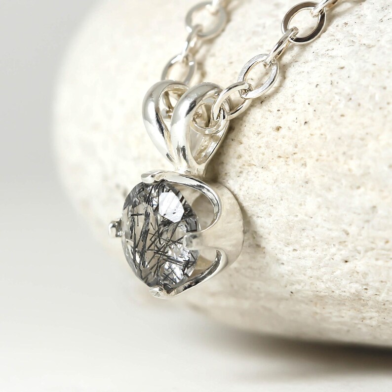 May include: A silver necklace with a pendant featuring a clear quartz stone with black inclusions. The pendant is set in a silver bezel setting.
