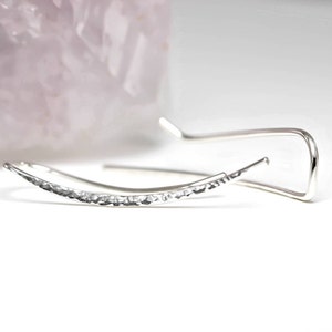 May include: A pair of silver hammered earrings with a curved shape. The earrings are simple and elegant.
