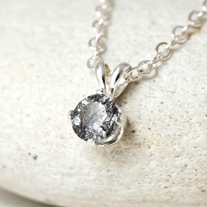 May include: A silver chain necklace with a round, clear quartz pendant with black inclusions. The pendant is set in a silver bezel.