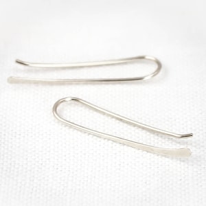 May include: A pair of silver hoop earrings with a simple, minimalist design. The earrings are made of thin, smooth metal and have a slightly curved shape.