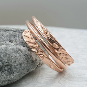May include: A rose gold ring with a textured, hammered finish. The ring is made of three bands that are twisted together.