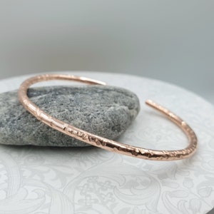 May include: A rose gold hammered bangle bracelet. The bracelet is simple and elegant, with a smooth, polished finish.