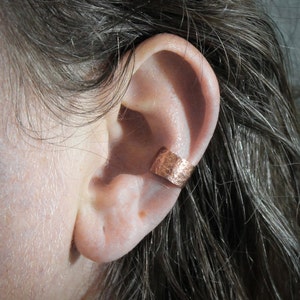 May include: A close-up of a person's ear with a copper ear cuff. The cuff is a simple band with a hammered texture.