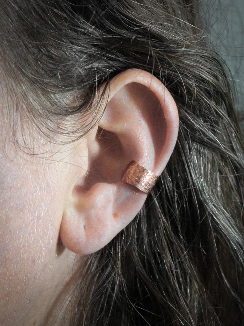 May include: A close-up of a person's ear with a copper ear cuff. The cuff is a simple band with a hammered texture.
