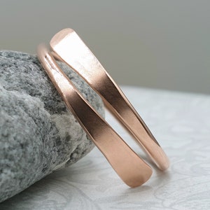 May include: A rose gold ring with a simple, minimalist design. The ring is made of two bands that are twisted together.