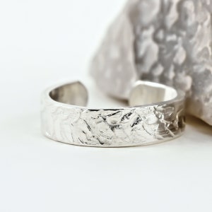 May include: A silver ring with a textured, hammered finish. The ring is wide and has a rounded shape.