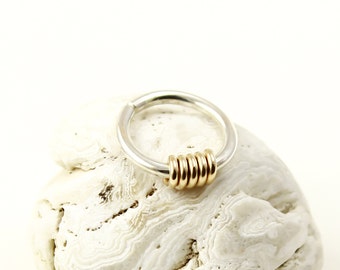 May include: A silver ring with a band of gold rings around it. The ring is sitting on a white rock.