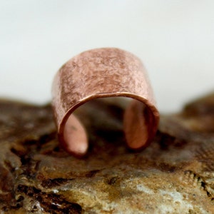 May include: A hammered copper ring with a rustic finish. The ring is open and has a wide band.