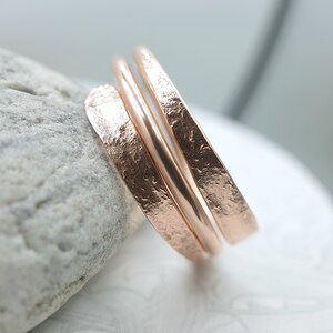 Puede incluir: Un conjunto de tres anillos de oro rosa con textura martillada. Los anillos están apilados uno encima del otro.