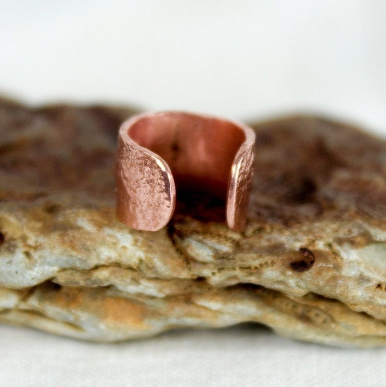 May include: A hammered copper ear cuff with a textured finish. The cuff is open on one side and is designed to fit snugly on the ear.