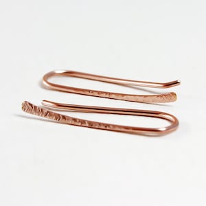 May include: A pair of rose gold hammered wire earrings. The earrings are simple and delicate, with a hammered finish that adds texture and dimension.