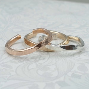 May include: Three hammered metal rings in different colors: rose gold, yellow gold, and silver. The rings are stacked on top of each other.