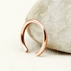 May include: A rose gold hammered hoop earring. The hoop is a simple, continuous circle with a hammered texture.