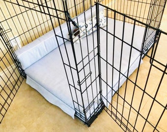 May include: A black metal pet playpen with a light blue dog bed and a patterned bolster pillow. The bed has a skirt and a matching bolster pillow. The playpen is on a light-colored tile floor.