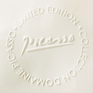 May include: A white ceramic plate with a raised embossed circle containing the text "Picasso" and the words "Domaine Picasso Limited Edition Collection".