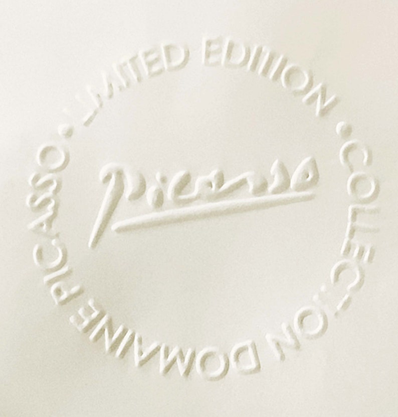 May include: A white ceramic plate with a raised embossed circle containing the text "Picasso" and the words "Domaine Picasso Limited Edition Collection".