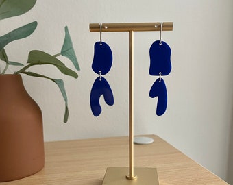 May include: A pair of blue abstract shaped earrings on a gold stand. The earrings are made of acrylic and have a modern, geometric design.