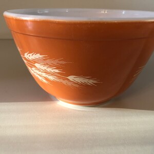 May include: A brown mixing bowl with a white wheat design. The bowl is made of glass and has a white rim.