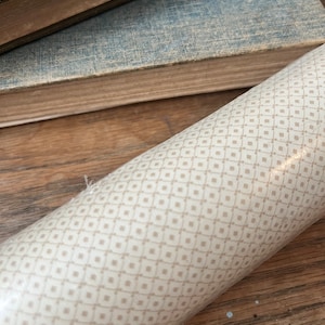 May include: A roll of white wallpaper with a beige geometric pattern of squares.