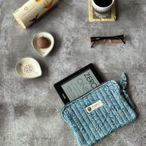 May include: A blue and white patterned fabric case with a zipper closure, holding a black Kindle e-reader. The e-reader is open to the title page of the book "Zero to One: Notes on Startups, or How to Build the Future" by Peter Thiel.