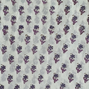 Op de afbeelding: Witte stof met een herhalend patroon van paarse bloemen. Elke bloem heeft meerdere bloemblaadjes en is verbonden met een stengel met bladeren. Het patroon is gelijkmatig verdeeld over de stof.
