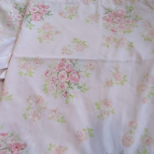 May include: A light pink fabric featuring a repeating pattern of soft pink rose bouquets and small green leaves. The floral design is distributed across the surface, showcasing clusters of blooming roses in varying shades of pink and white.