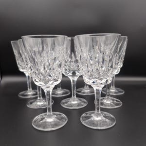Può includere: Un set di calici da vino in cristallo trasparente con un dettagliato motivo a taglio diamante sulla coppa, uno stelo liscio e una base circolare. I calici sono disposti in gruppo, mettendo in risalto le sfaccettature riflettenti.