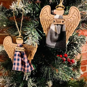 May include: Two wooden angel ornaments with wings, a halo, and a plaid fabric bow. The ornaments are hanging on a Christmas tree. One ornament has the name "Papa" on it, and the other has the name "Grandpa" on it.