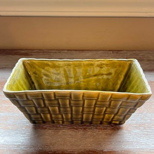 May include: A green ceramic planter with a woven design. The planter is square shaped and has a wide opening.