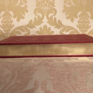 May include: The spine of a red hardcover book with a decorative pattern and a cream-colored page edge.