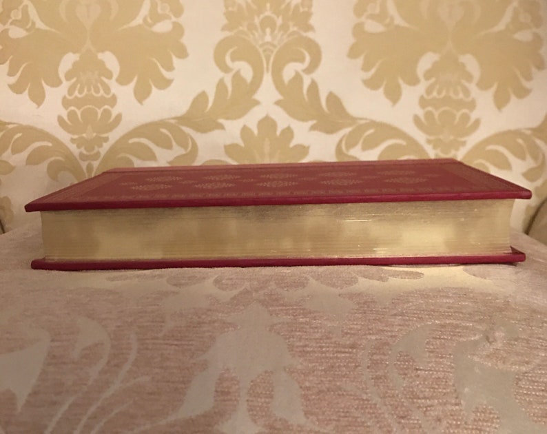 May include: The spine of a red hardcover book with a decorative pattern and a cream-colored page edge.